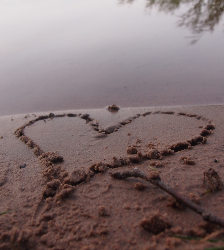 Hiekkaan piirretty sydän rantahietikossa.